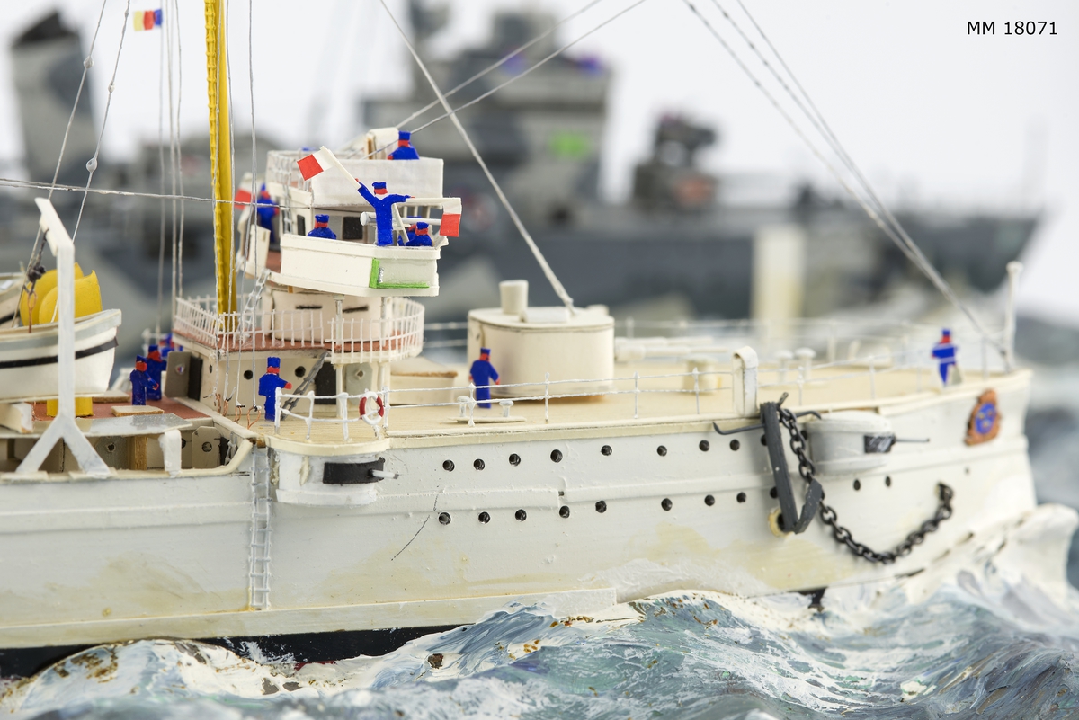 Fartygsdiorama visande två fartyg under gång till sjöss. Modellen är tillverkad av trä med detaljer av plast, papper och metall. Modellerna är placerade i ett hav av någon form av plastelina, målat i gröna och blå toner. Havet är uppbyggt på en rektangulär platta. Modellerna är detaljerat återgivna och visar pansarkryssaren "Fylgia", den ena modellen visar fartyget i sitt ursprungliga skick, den andra modellen visar fartyget efter moderniseringen 1939-40. Den "äldre" modellen visar ett vitt fartyg med rök bestående av grå ull från de tre skorstenarna, den "yngre" modellen visar ett kamouflagemålat fartyg försett med vitt neutralitetsband. Dioramat är signerat på havet med rött: "H Biärsjö".