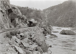 Et lokomotiv med vogner, jernbaneskinner ved en gruve.