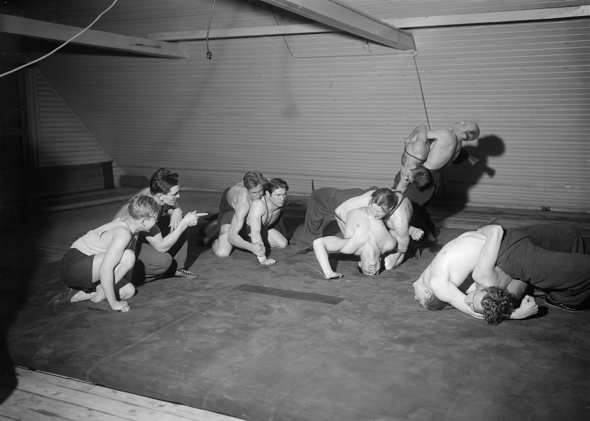 Brottarträning i gymnastiksalen på F 3 Malmen, 1943. Fyra brottarpar under övning, två män tittar på.