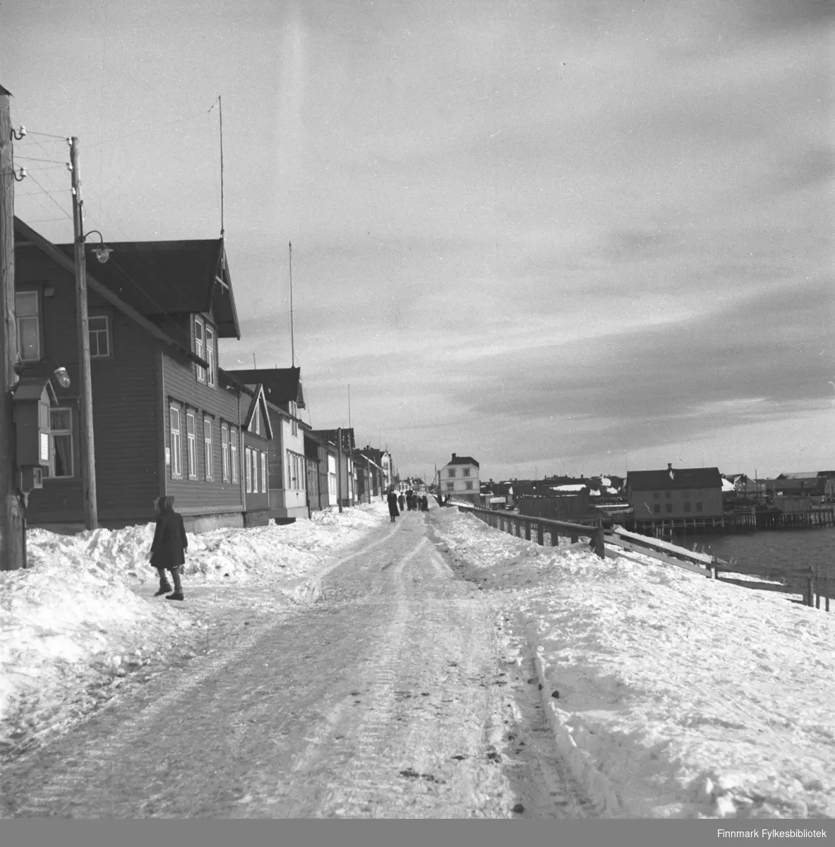 Fotografi fra Vadsø. Havnegata mot øst.  Til venstre i bildet går lærer Megrund. Bak ham sees Johannes Helfjords hus. I enden av gata skimtes Evangergården. Bildet er tatt før krigen. Fotograf ukjent.