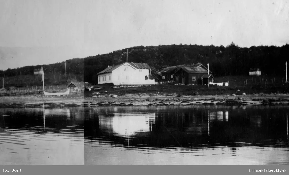 Gården Strømsnes i Jarfjord, bildet tatt fra sjøsiden. Bildet er muligens tatt i 1923. Husene på gården brente ned i 1947. På bildet kan man se fjæra og havet ved siden av bygningene og i bakgrunnen kan man se et lite fjell med skog på. Rundt om kring har det blitt satt opp gjerder og man kan se enkelte strømlinjer på området. Til venstre side av bildet kan ma se en båt på land.