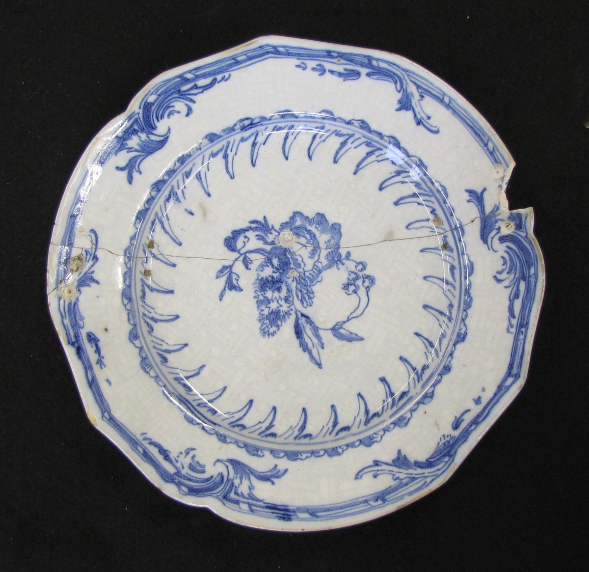 Tallrik av fajans med ''Rehnska mönstret'' i blått, komponerat av Jean Eric Rehn, på bianco sopra bianco-botten (blågrå botten med vitt mönster).


 Rehnska mönstret består av "en sinnrikt och rytmiskt svingad rokokobordyr och därtill ett centrumstycke i form av ett blomster- eller fruktmotiv, som liknar ett söndersprunget granatäpple." 

Citatet ovan är hämtat från Hannover, Emil "Keramisk handbok. Första delen. Fajans - majolika - stengods" (Stockholm 1919), s. 467 - 468. På s. 468 i samma bok står bl.a. följande: "Första gången rokokobordyren uppträder är på en servis från 1745. Där är granatäpplet ersatt av Adolf Fredriks namnchiffer med en krona över. Också med olika adliga vapen i stället för granatäpplet förekommer det Rhenska mönstret, som överhuvud taget finns varierat på mångahanda sätt. Det uppträder så t.ex. manganmålat i stället för blåmålat och som blåmålat ofta på sopra bianco-botten. I bortåt trettio år upprepades det oupphörligt i Rörstrands fabrik - märkvärdigt nog utan att mista synnerligen mycket av sin rena och vackra rokokokaraktär."

Signerad: St. 2/5 1762

                    16......(?)

Tallriken sprucken och lagad med krampor. Bitar slagna ur kanten men fastlimmade. Tallriken inköptes

av ägarens far Christian Aarsrud (18 - 19) disponent vid Mustafors, Dalsland.



Bilaga: Värderingsintyg'