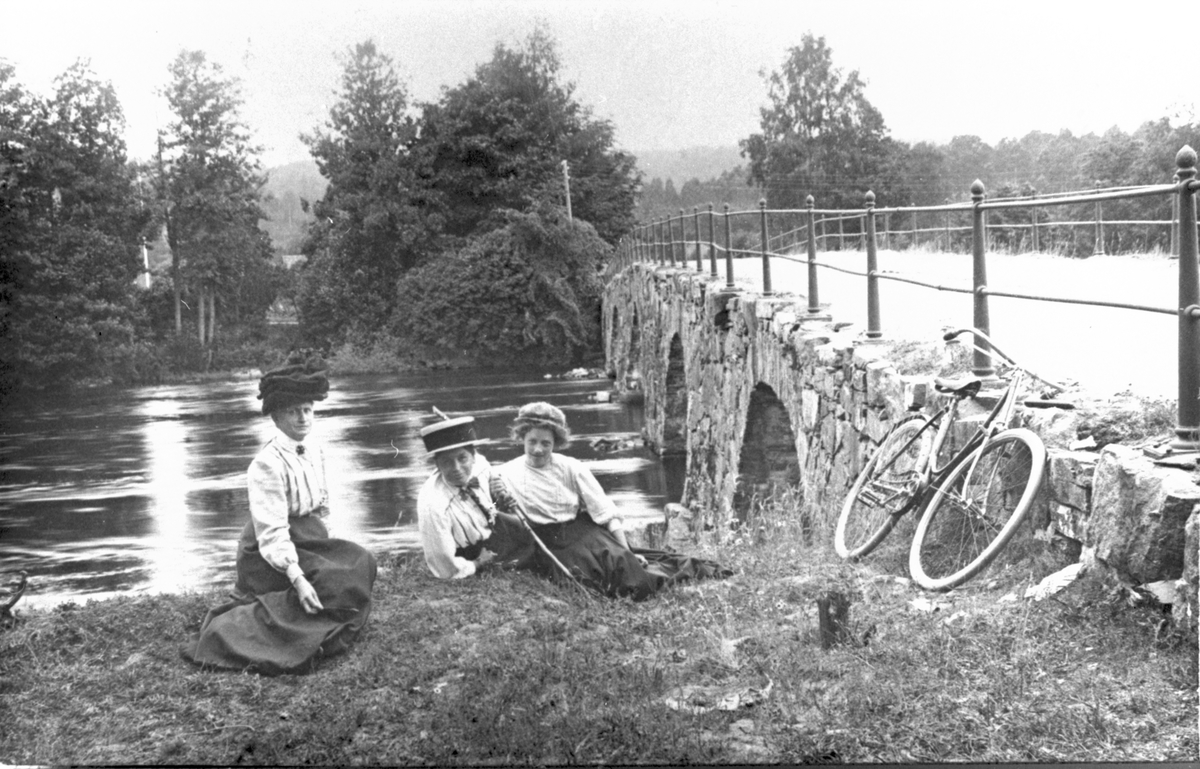 Kvinnor på cykeltur vilar i gröngräset vid vattnet.