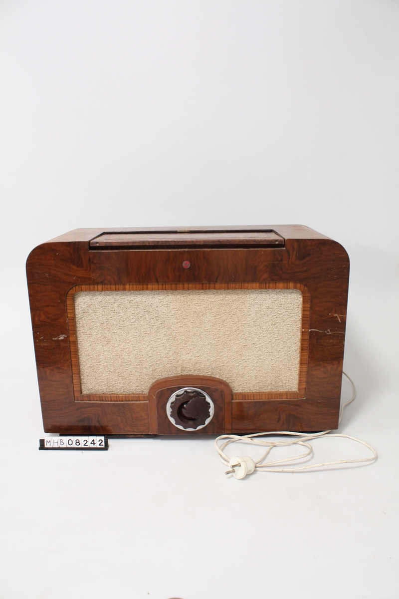 Philips radioapparat fra omkring 1939. Trolig kjøpt hos Brommeland. Innlevert til tyskerne under krigen. Plate på toppen dekker søkerskala som kan vippest opp. Nederst midt i front en skruknott for innstilling av frekvens.