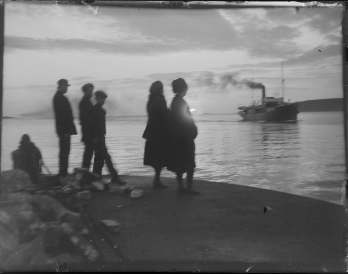 Reisende står på kaia i Vardø og venter på hurtigruta som snart legger til. Et stemningsbilde med midnattsol