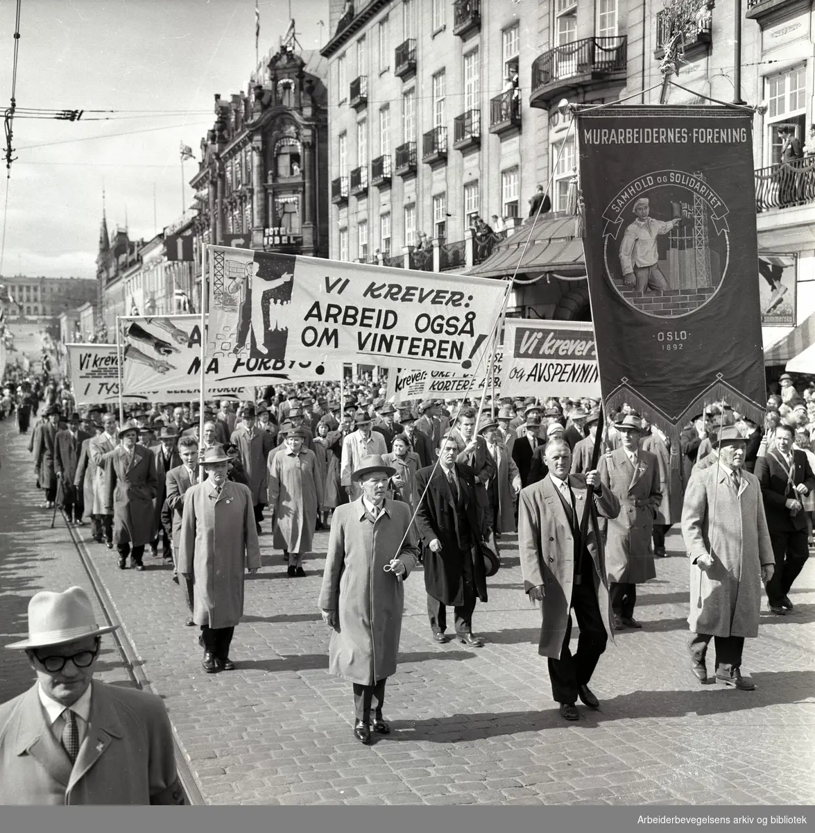 1. mai 1958 i Oslo.Demonstrasjonstoget på Karl Johans gate.Fane: Murarbeidernes forening.Parole: Vi krever arbeid også om vinteren!.