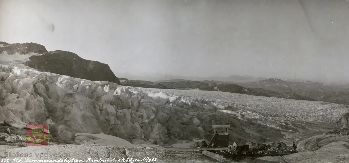 Album fra 1903-1908. Ved Demmevasshytta. Rembedalsskåkjen. På bildet ser vi isbreen og pipa på det lille murhuset ved Demmesvasshytta.  10.08.1908.