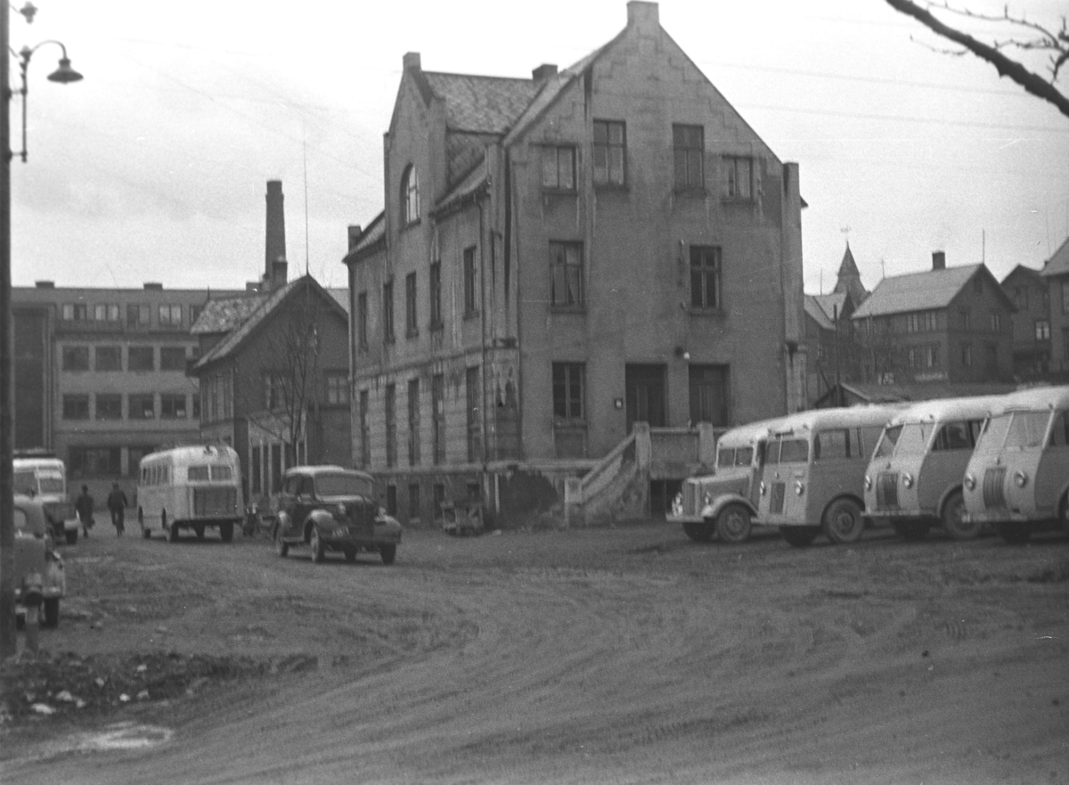 Bilde av et gateparti med noen busser parkert utenfor en stor bygning. Stedet er ukjent, men kan være Harstad.