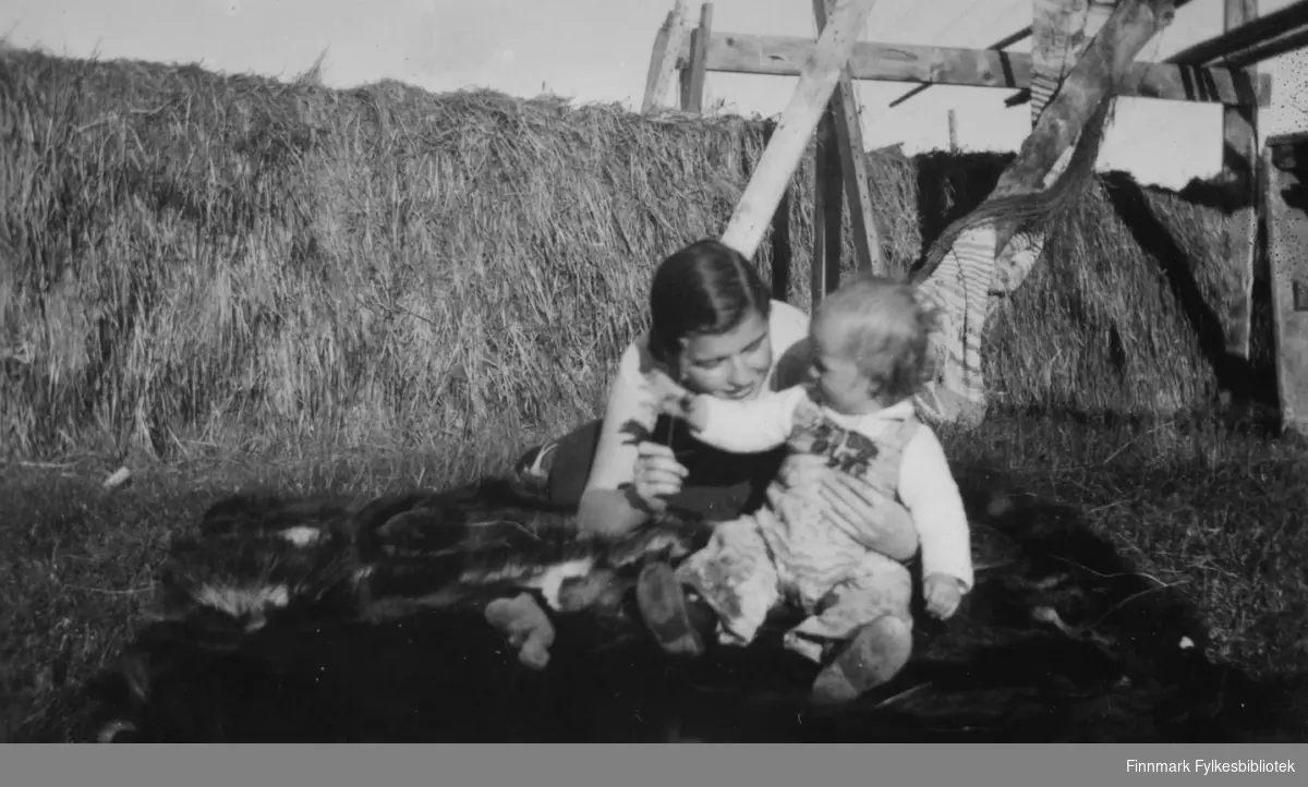 Solveig Evanger leker med Pia Gunnari på et dyreskinn, sommeren 1935. I bakgrunnen fulle høyhesjer.