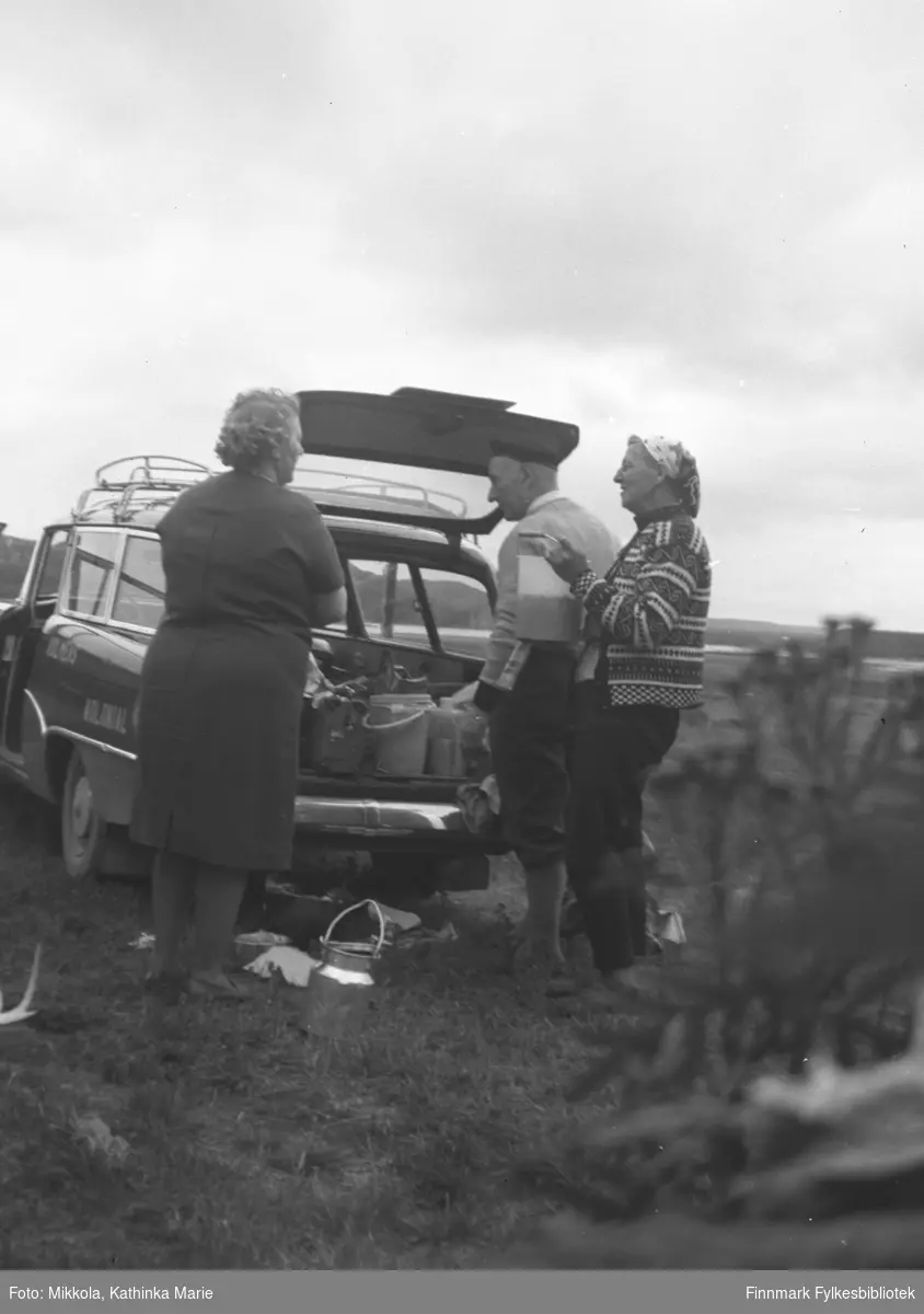 Ekteparet Holm fra Bodø var på besøk på Mikkelsnes, ca. 1962-1965. Her ser det ut til at de har vært på multebærtur i Neiden-området. Bærspann og annet utstyr blir lastet inn i bilen. Til venstre: Gudrun Olsen Lie