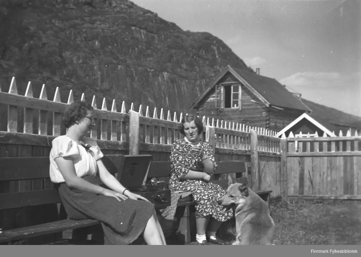 Søstrene Ingrid (til venstre) og Astrid Mikkola med sveivegrammofon i hagen på Mikkelsnes en sommerdag. Gårdshunden var også musikkinteressert