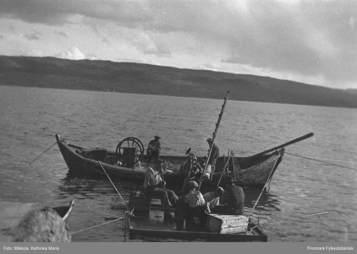 Bygging av dampskipskaia ved Mikkelsnes i Neiden, ca. 1935-1937. Her dykker O. Sundquist ved kaia på Mikkelsnes. Hjulet på båten ble brukt til å pumpe luft til dykkerne. To personer måtte sveive for å pumpe luft ned til dykkerne. På dette bildet kan det være Tobias Labahå som sitter ved sveiva. Stigen som står oppreist mellom flåten og båten ble brukt av dykkerne under opp- og nedstigning