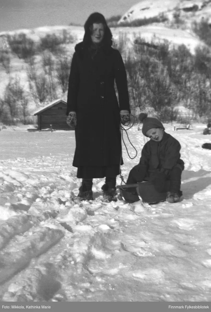 På kjelken Astrid Mikkola, søsteren Marine står i snøen ved siden av. Begge har skaller på bena, og Marine har fine selbuvotter
