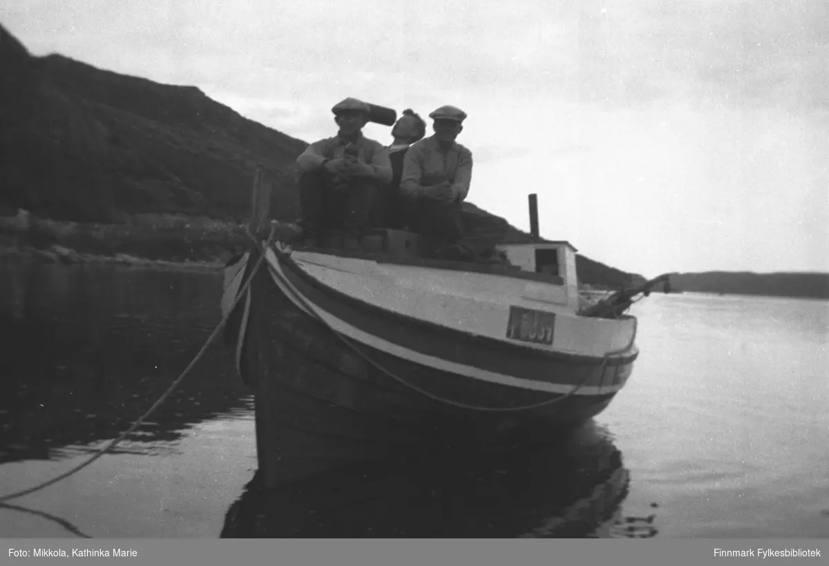 Mindre motorbåt fortøyd ved sjøsiden på Mikkelsnes. Båten har registreringsnummer F63SV. Tre menn sitter ombord, to av dem med flasker. Fra venstre: Arvid, Storm og Leif Mikkola. Bildet har en rolig stemning av avslapning etter strev