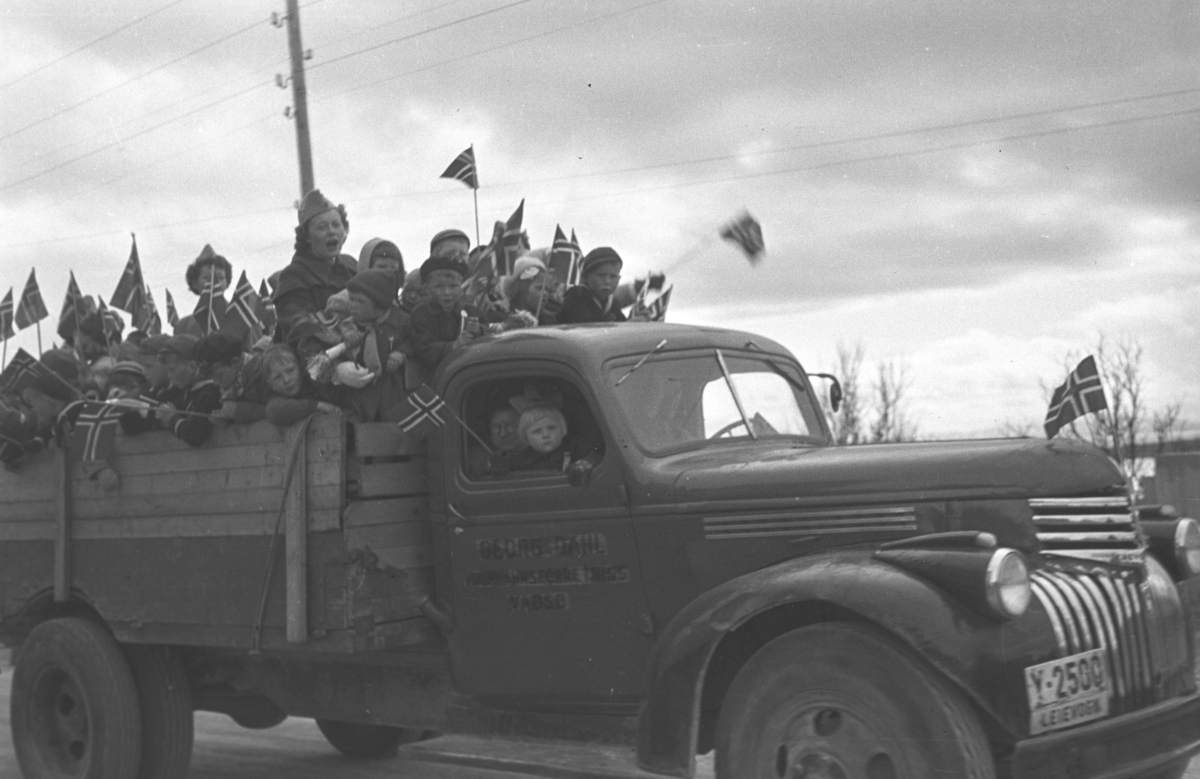 17. mai-feiring i Vadsø. Lotter er satt til å passe barna som er samlet på lasteplanet til en Chevrolet 1946-47 mod. mens de vinker med norske flag.