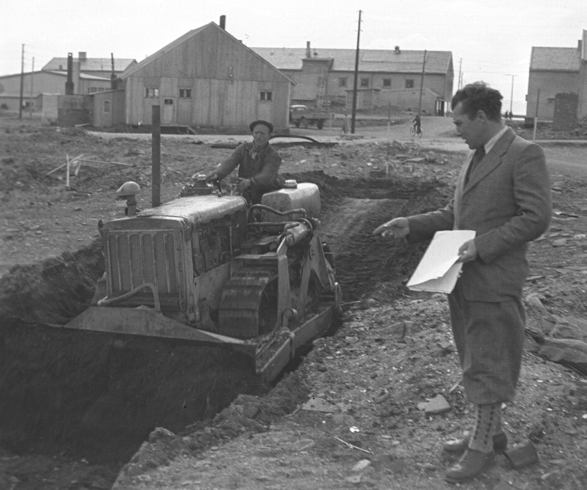 En bulldoser er begynt å grave ut tomta til Vårbrudd i Vadsø. Mannen som står med noen papirer i hånda er Alfred Bjørkli. Føreren av maskinen er ukjent.