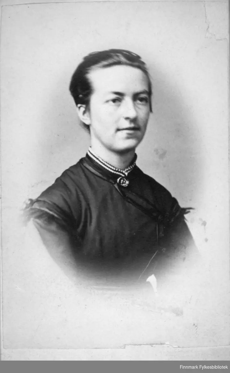 Portrett av en dame med kort, bakovergreid hår. Hun har en mørk bluse på seg og et smykke rundt halsen. Portrettet er tatt hos H. Ulseth i Bergen.