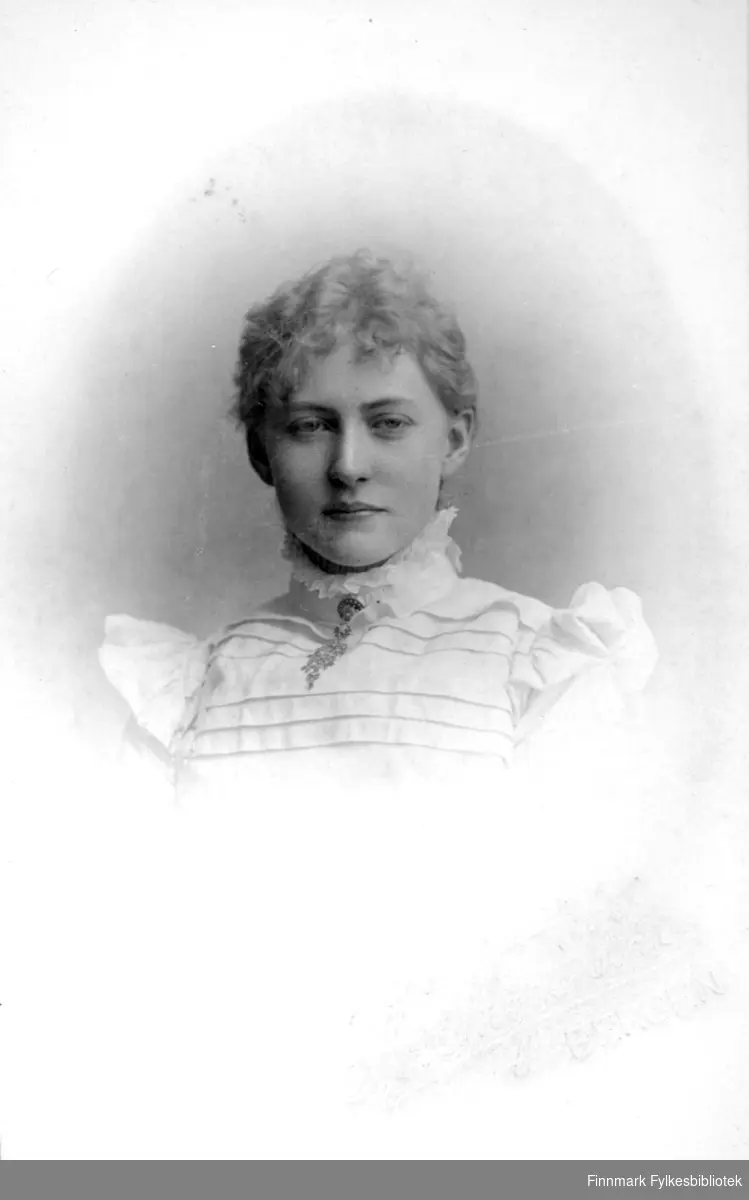 Portrett av en kvinne iført en lys bluse med noen striper foran og volanger.