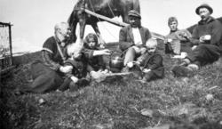 Syv personer, tre barn og fire voksne, sitter rundt et bål m