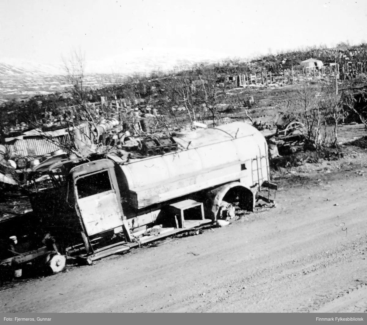Bilde fra Lapplandsarmeens retrettvei. Vraket av en lastebil står i veikanten og ruiner av flere bygninger ses i bakgrunnen. Nøyaktig sted er ukjent.