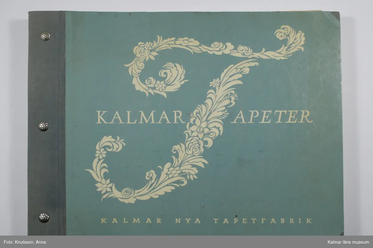 KLM 28100:2. Tapet, tapetkatalog. Grön pärm i kartongpapper med tryck: Kalmar Tapeter, Kalmar Nya Tapetfabrik. Katalogen innehåller tapetprover i olika färger och utförande. Datering: 1950-tal.