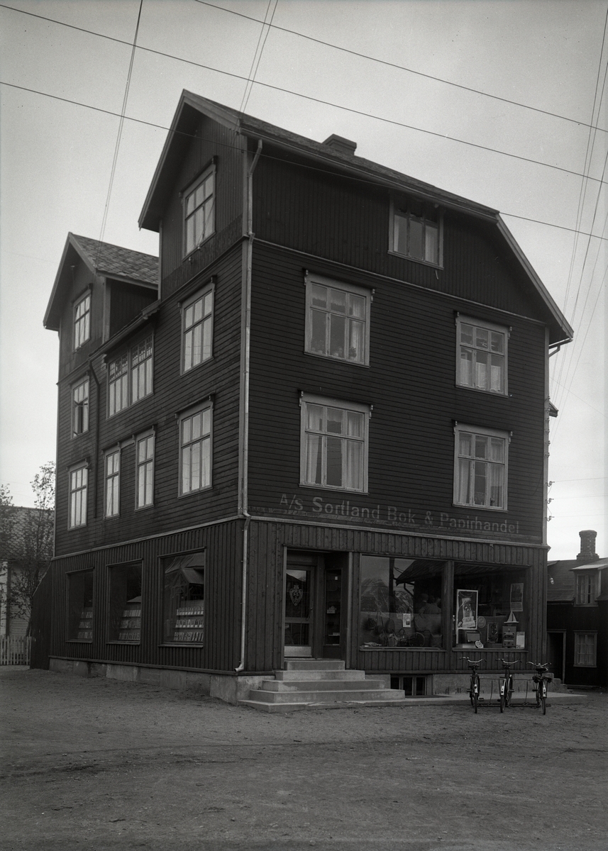 Sortland Bok & Papirhandel i Heidenstrømgården (Bokhandlergården) ca. 1950. Bygningen ble satt opp i 1920 av Reidar Heidenstrøm, som var direktør ved Vesteraalens Hermetikkfabrikk. Den ble brukt til bolig og ulike forretninger. Bl.a. hadde fotograf Lind atelier der.
