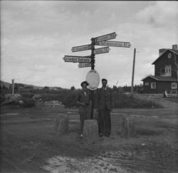 To unge menn står ved et finsk veiskilt. Ved et veikryss.