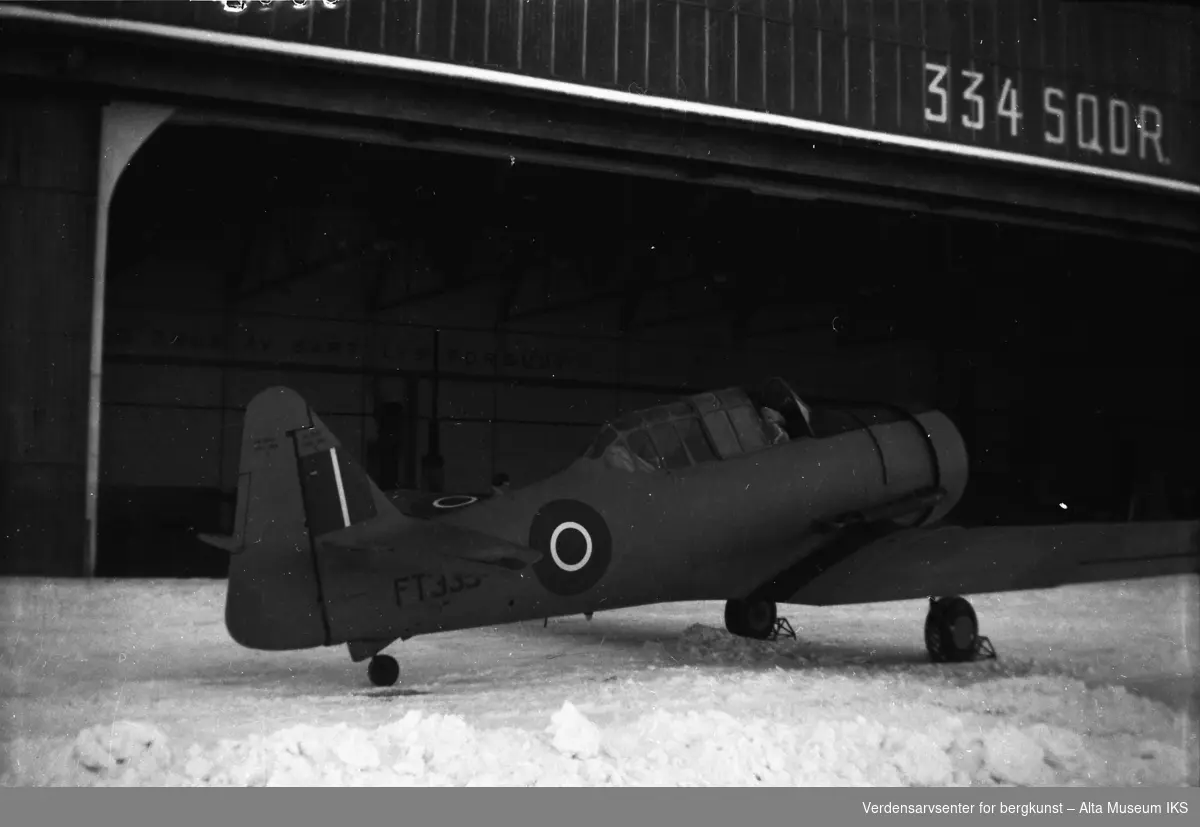 Et militært fly står i snøen utenfor hangaren. På hangaren står det 334 SQDR med store bokstaver.
 Bildet er tatt vinteren 1949.
