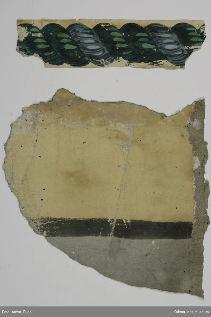 KLM 17319. Tapet, målad tapet av papper. Målad med gult limfärgsfält, avgränsat upptill av svart streck. Nertill gråmålat fält. Överst har en tryckt bård suttit, repliknande motiv i grönt och grått på gulfärgad botten. Datering: 1810-1830-tal.