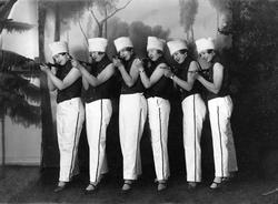 Seks kvinner i kostymer på en scene.