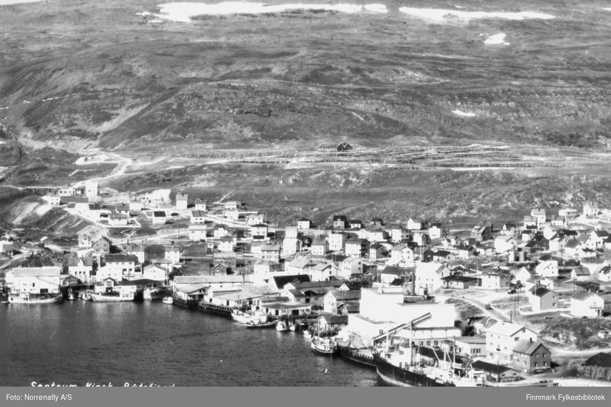 Oversiktsbilde av Båtsfjord. Påskrift på bildet: "Sentrum Kiosk, Båtsfjord".  Helt til høyre ved kaia ligger Vesterålskes godsbåt "Senja". Bildet er trolig tatt i siste del av 1900-tallet. (1950?)