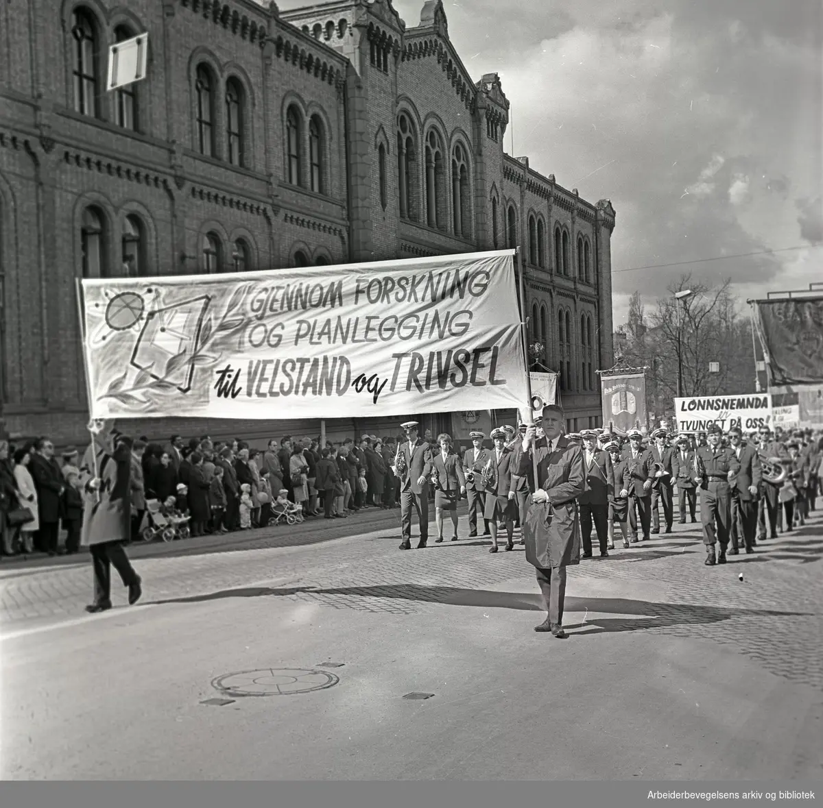 1. mai 1964 i Oslo.Demonstrasjonstoget i Karl Johans gate.Parole: Gjennom forskning og planlegging til velstand og trivsel.Parole: Lønnsnemda er tvunget på oss!