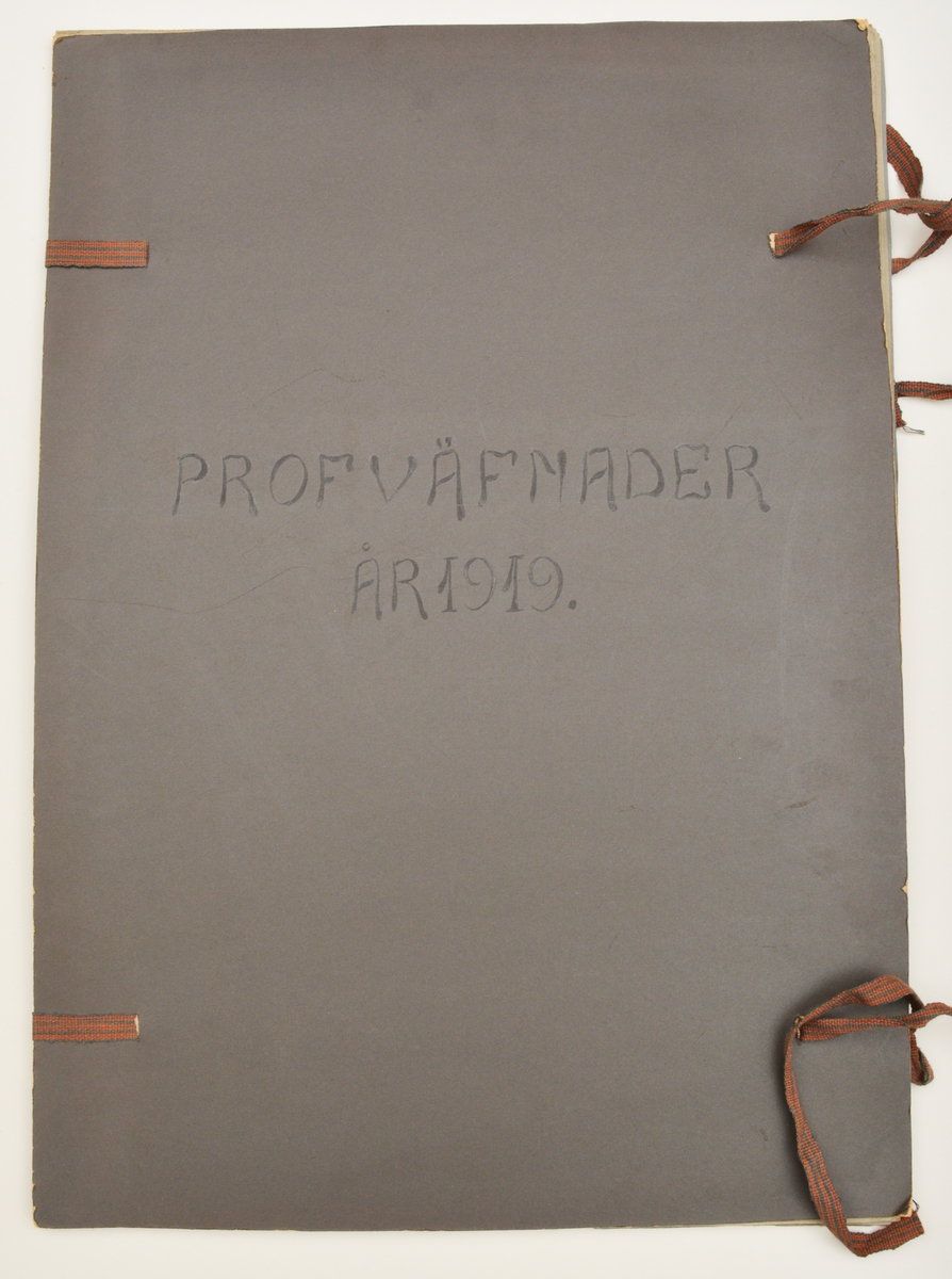 Stor pappersmapp med lösa blad med påklistrade tygprover. Pärmarna är av en annan papperskvalité än papperna innuti. Pärmarna hålls ihop med ett par långa, handvävda band.
Text på framsidan; "Väfprofer År 1919".