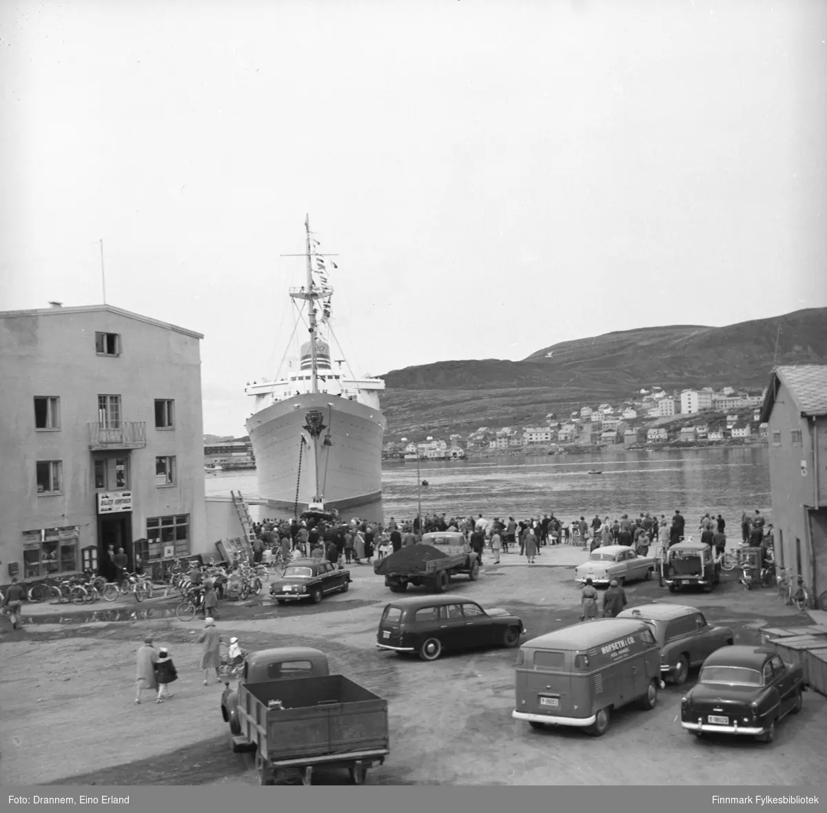 Passasjerskip nærmer seg Hammerfest havn, folk står ved kaia og venter. Flere biler er parkert i nærheten av kaia
