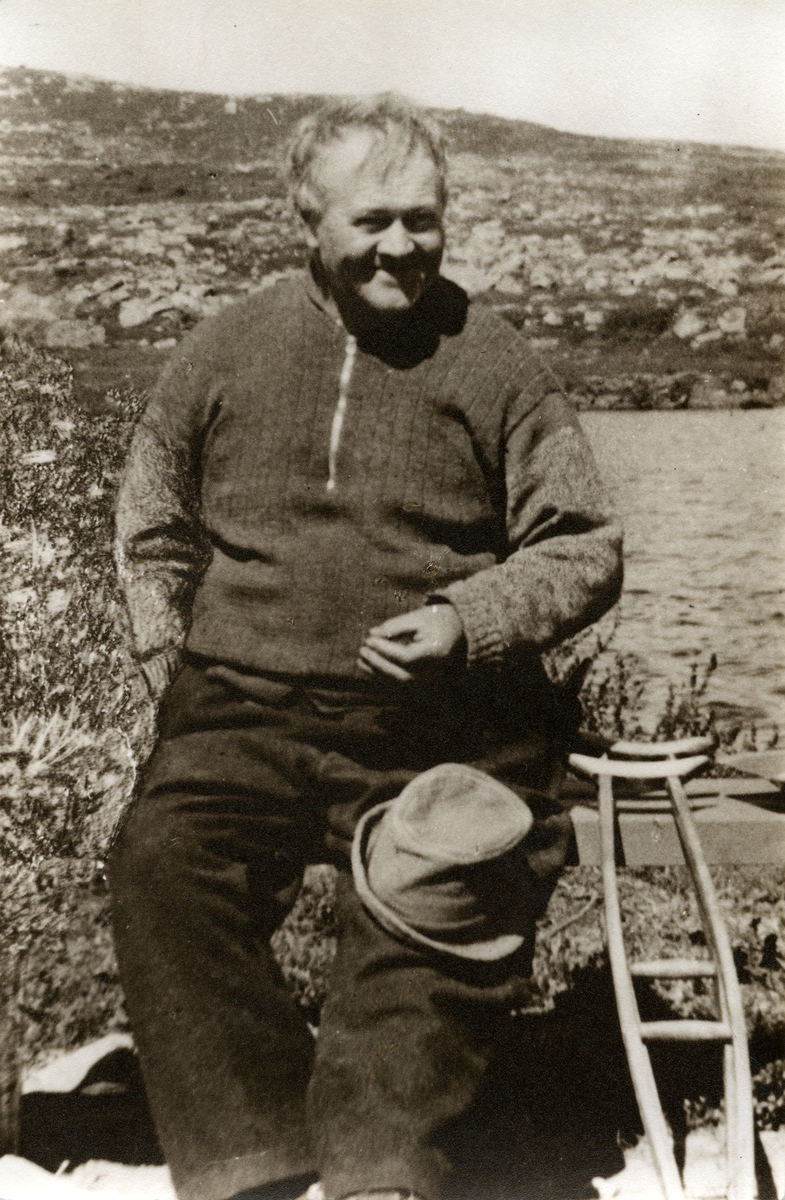 Portrett av en mann sittende på en benk. Mannen har en hatt på kneet og en krykke plassert ved siden av.