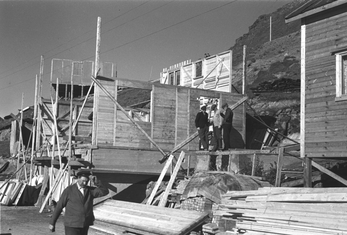 Bygningsarbeidere er i gang med å sette opp et gjenreisningshus i Honningsvåg en sommerdag i 1946.

Arkitekt Ola Hanche-Olsen arbeidet ved Brente Steders Reguleringskontor i 1946. Hovedadministrasjon for gjenreisning av Nord-Troms og Finnmark ble lagt til Harstad og fikk navnet Finnmark kontoret. Landsdelen Nord-Troms og Finnmark blev oppdelt i syv distrikt med hver sin administrasjon. Honningsvåg, distrikt IV, skulle betjene Nordkapp, Lebesby, Porsanger og Karasjok kommune.

Ola Hanche-Olsen har tatt bildene. Han var født 13. mars 1920 i Borre, død 11. februar 1998 i Gjettum. Han var både arkitekt og barnebokforfatter. Han hadde artium fra 1939, arkitekteksamen fra NTH 1946 og arbeidet deretter ved Finnmarkskontoret 1946–48 før han etablerte egen arkitektpraksis. Han debuterte som barnebokforfatter i 1974 med lettlest-boka "Knut og sjørøverne", og skrev i alt 12 bøker. Han var XU-agent 1944-45, og var også en aktiv fjellklatrer og friluftsmann. Ola var gift med Solveig Hanche-Olsen (f. Falkenberg); de fikk 3 barn, blant dem matematikeren Harald Hanche-Olsen.

