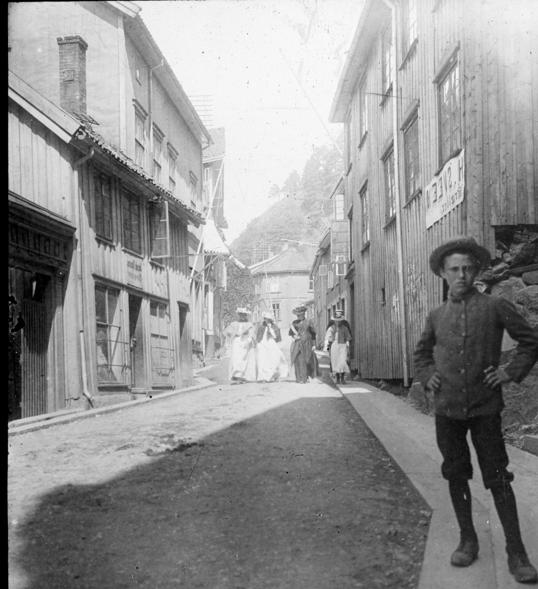 Fra Kirkegaten, gutt med knebukser og hatt i forgr., fire velkledte kvinner promenerer bak. før 1900 tallet. Kragerø