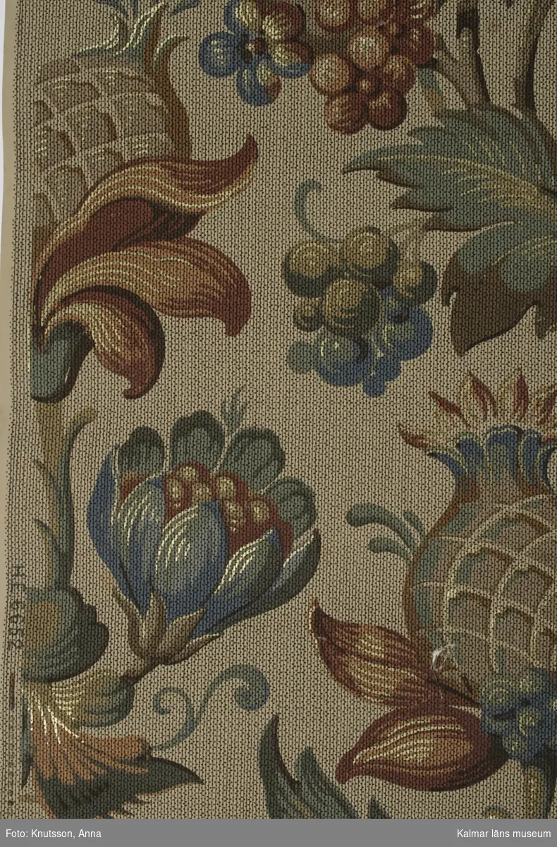 KLM 39847. Tapet i papper. 1 rulle. Stora blommor i textilliknande mönster. Mustiga färger i blått, grönt, rött, brunt och orange. Tryckt på kanten: HE 6652. Stämplat på baksidan: SMÅLANDS MUSEUM VÄXJÖ. Datering: 1890-1910-tal.