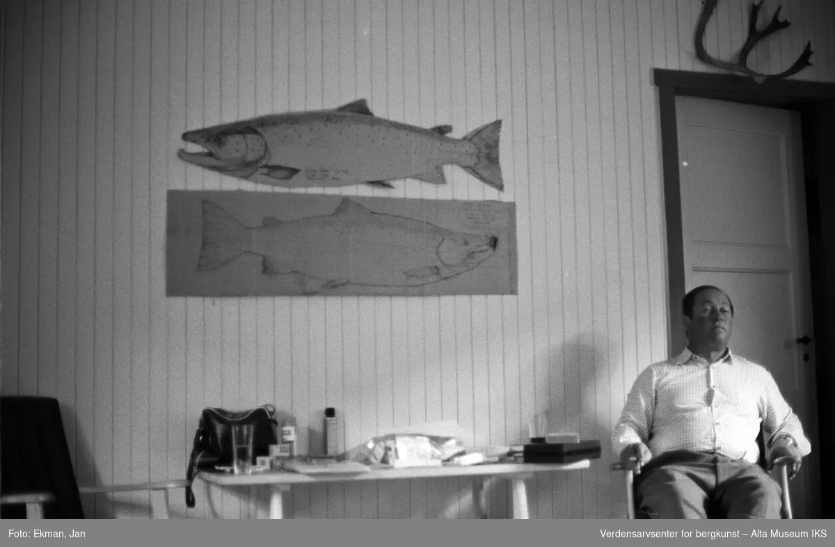 Hytteinteriør med personer.

Fotografert mellom 1975 og 1976.

Fotoserie: Laksefiske i Altaelva i perioden 1970-1988 (av Jan Ekman).
