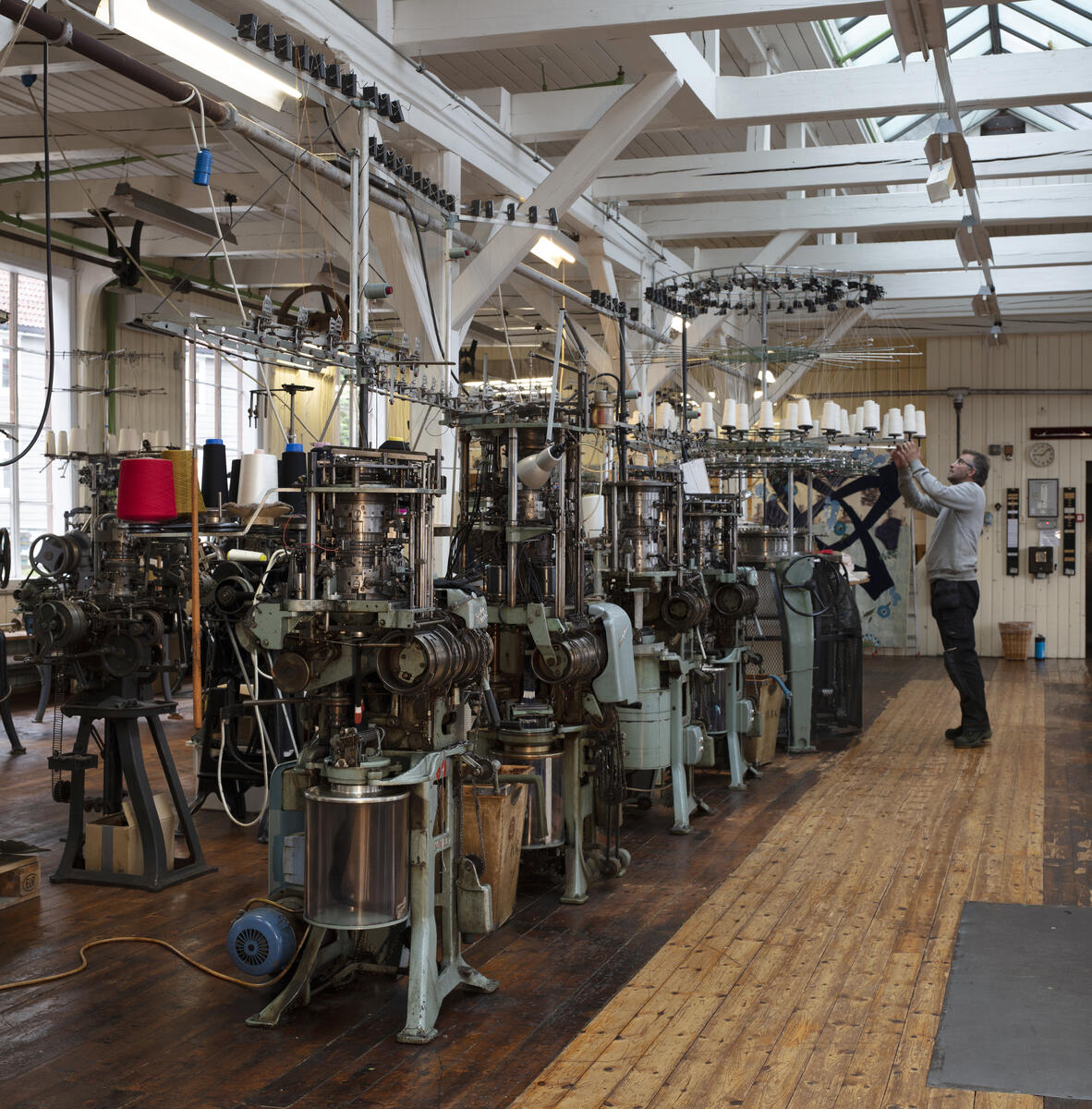 strikkemaskiner i fabrikklokale, mann arbeider med maskin