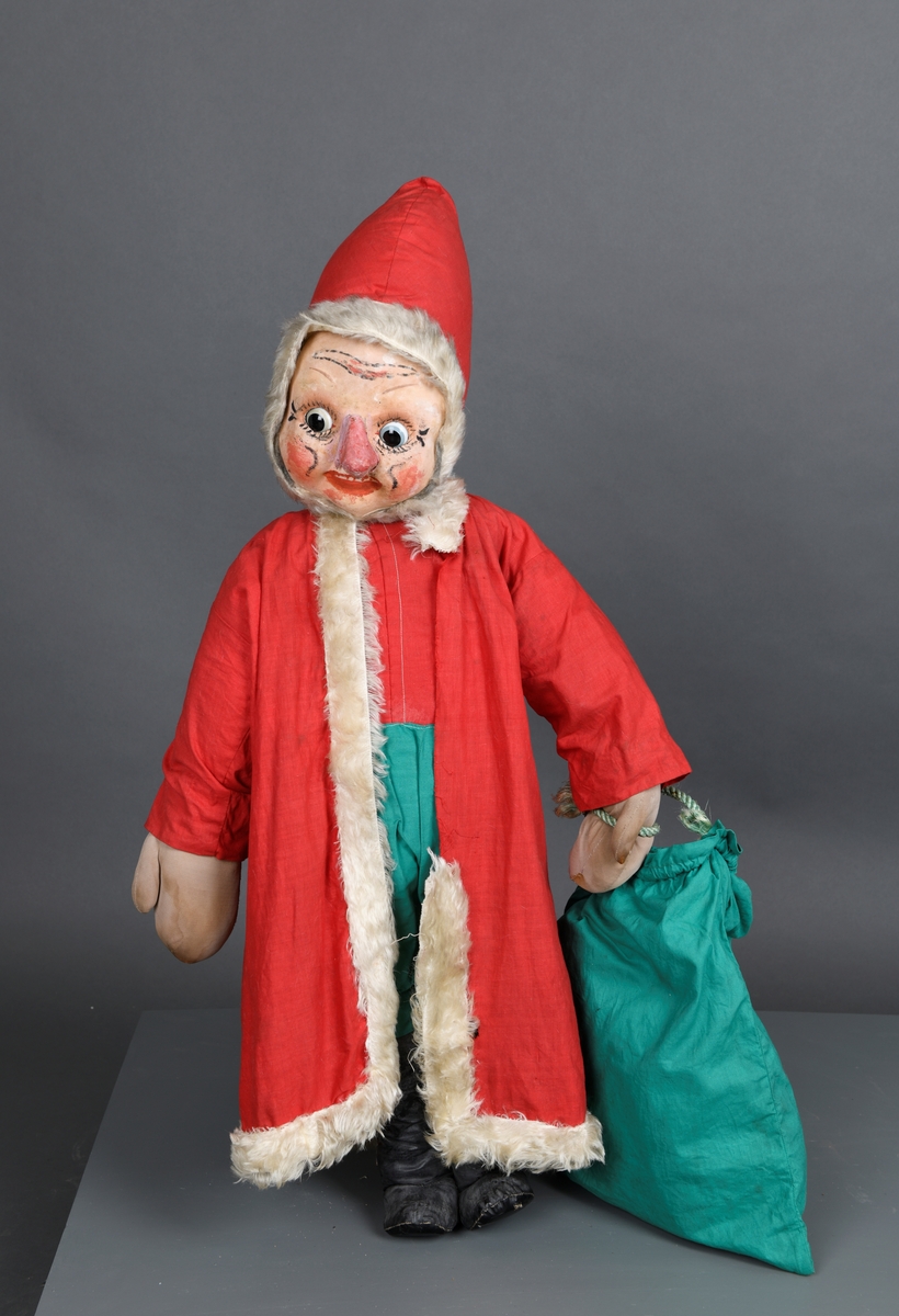 En julenisse brukt til julepynting i skobutikk (Edvin Kvernø) i Trondheim. Hodet har spiss lue sydd av rødt bomullsstoff. Rundt åpningen for ansiktet er det sydd på en hvit kant med fuskepels. Ansiktet er en maske av myk papp/stoff som er festet på hodet/i luen. Det er påmalt rynker i pannen, øyevipper/bryn, røde kinn, rød munn og rød nese. Han har øyne av plast, et blått og et brunt. Øynene kan bevege seg fra side til side. Hodet er festet til kroppen med en trestang. Kroppen er trolig laget av noe plast og tykk ståltråd. Kroppen er også trolig fylt ut med vatt eller lignende. Klærne er sydd på med maskinsøm. Nissen har rød skjorte, grønne bukser og rød frakk. Langs kanten på frakken er det sydd en kant med hvit fuskepels. Den er sydd på for hånd. På beina har han svarte knehøye støvler laget av svart plastbelagt lerret. Hendene/vottene er maskinsydd av grått nylonstoff. Det er ståltråd og vatt i hendene. I den ene hånden har han en gavesekk sydd av grønt bomullsstoff. Sekken har håndtak av grønt nylontau.