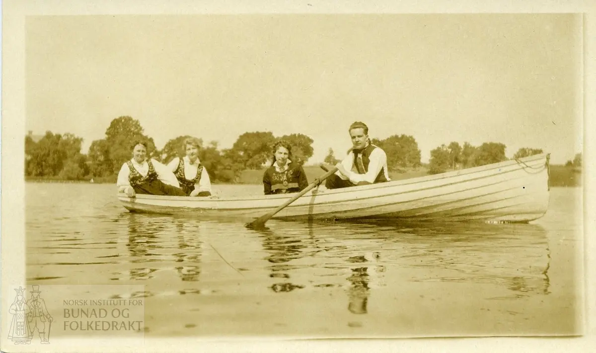 3 kvinner og en mann i bunad - i en robåt.