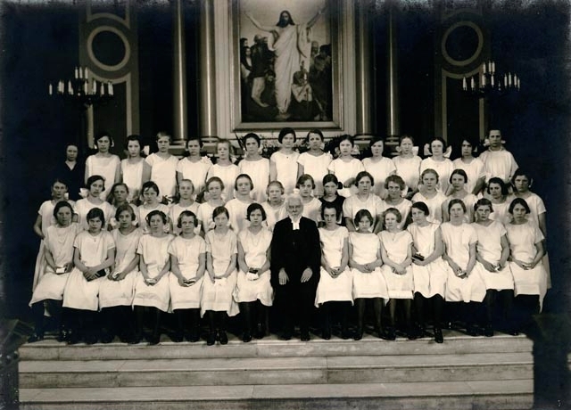 En grupp konfirmander, flickor, med präst sitter i kyrkan.