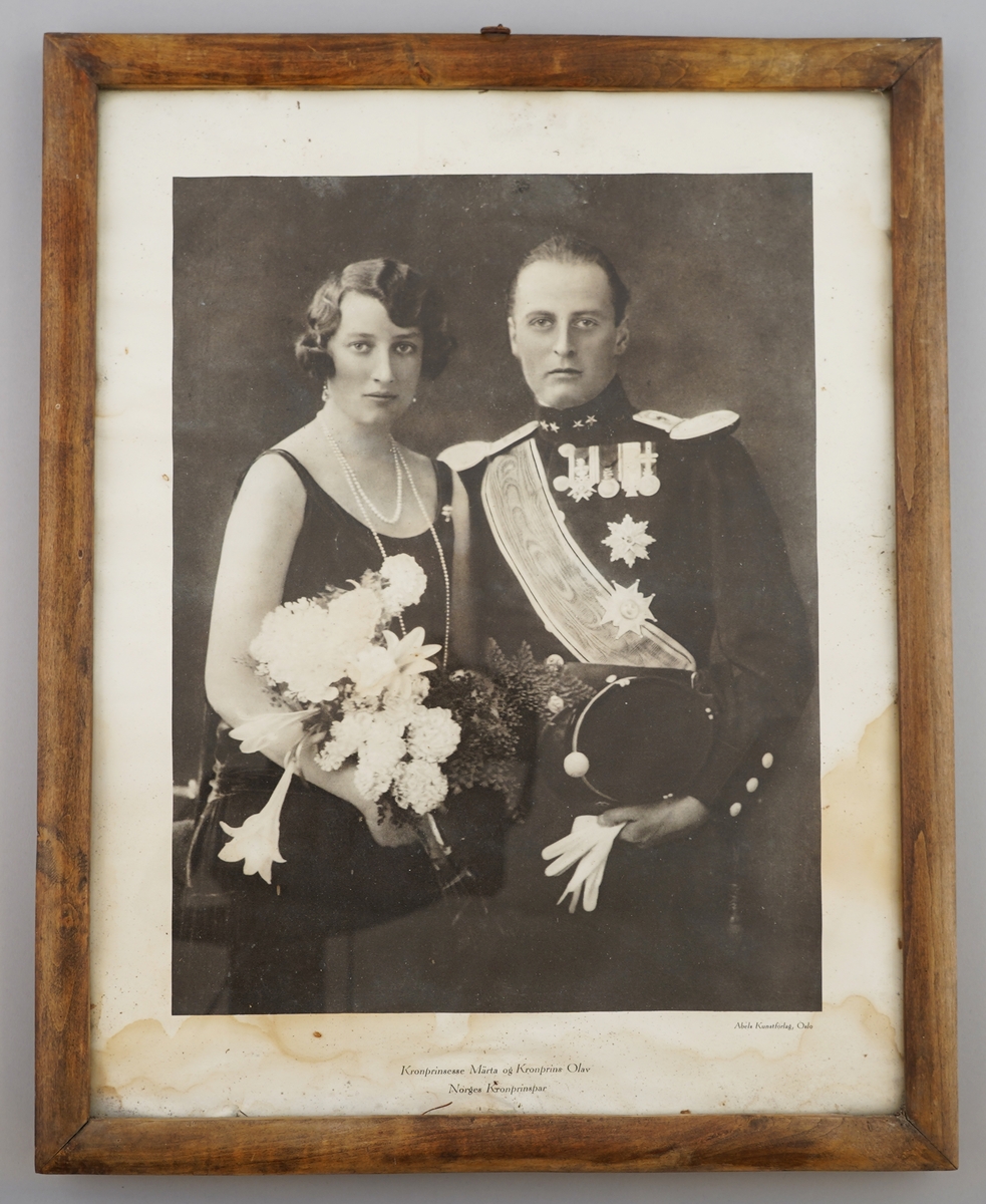 Innråma svart-kvitt-foto (reproduksjon) av kronprinsesse Märta og kronprins Olav. Råma er av tre og har ein liten metallring som oppgeng.