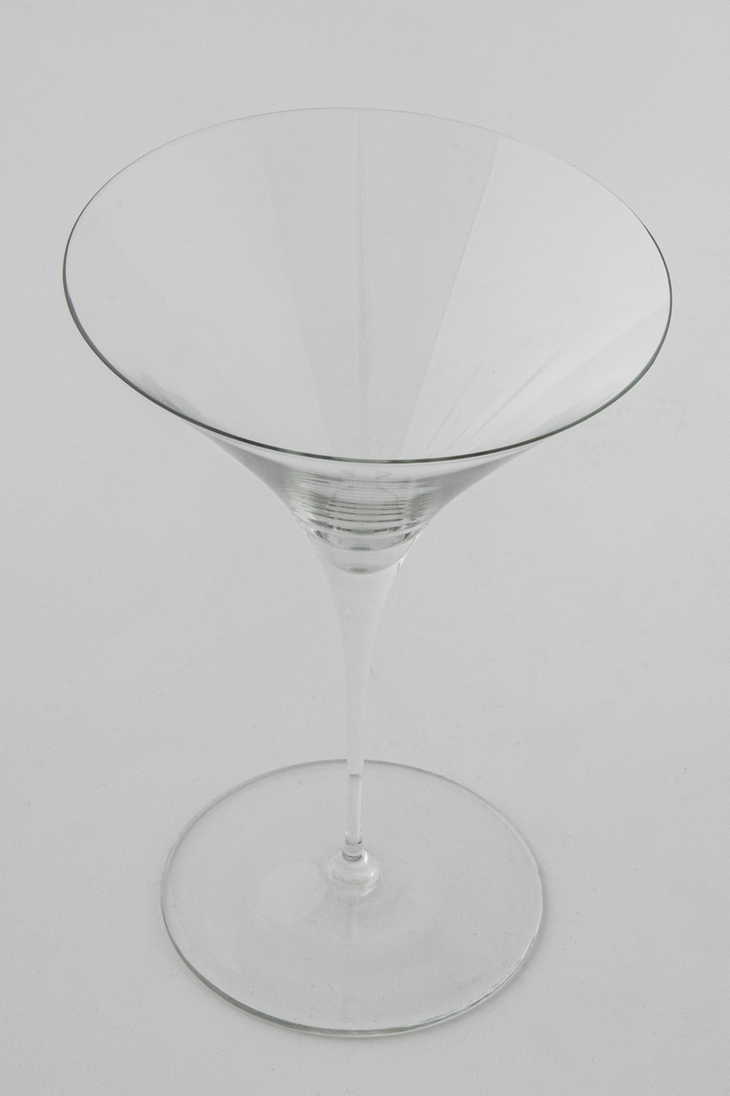 Champangeglass i klart glass. Konisk trumpetformet kupa som glir over i en stett, som hviler på en sirkulær fotplate.