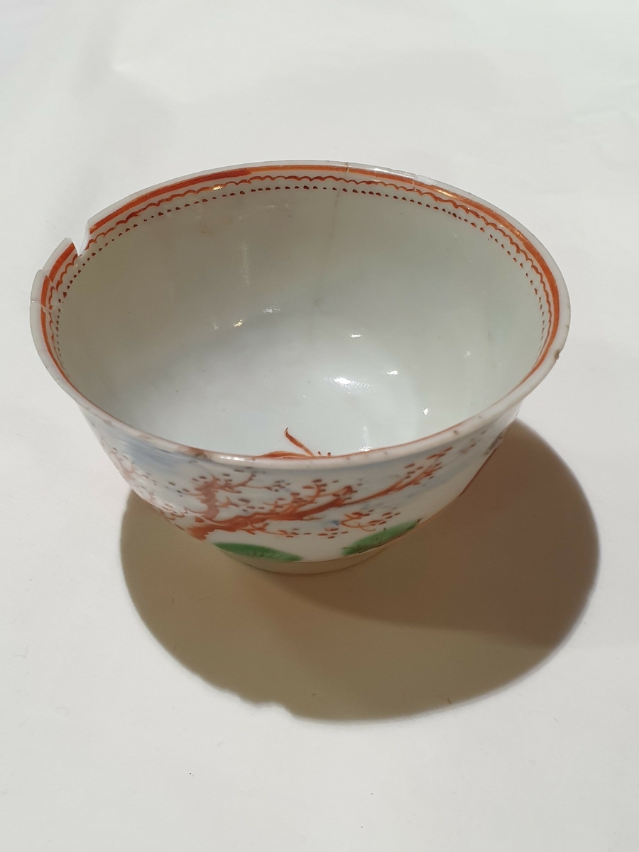 Kopp av glassert keramikk, med håndmalt dekor. Hvit grunnfarge, med flerfargede kineserier med motiv av mann med børtre. På innsiden av koppen går det en dekorativ, oransje borde.