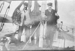 Portrett av tre menn på båtdekk, delvis skjult bak opphengte