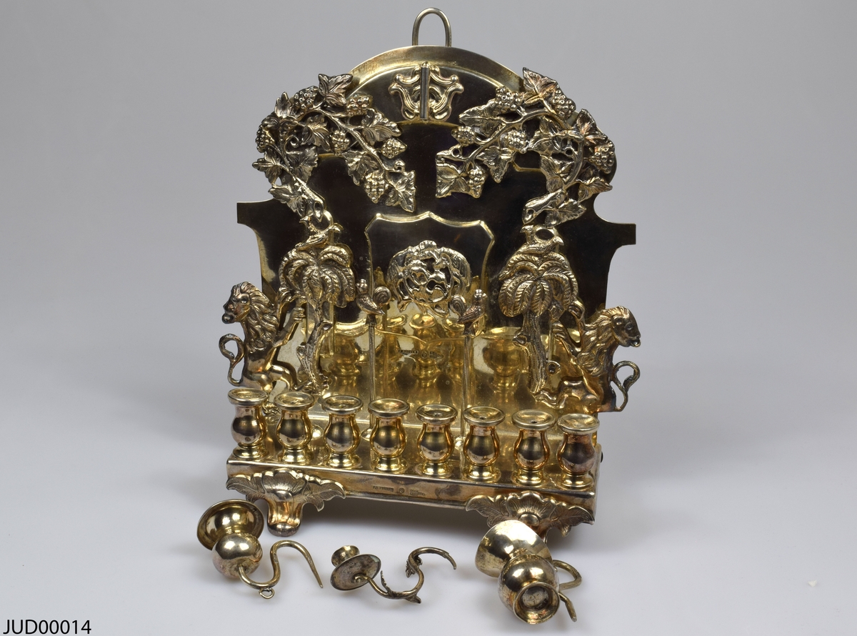 Silverchanukia med tre lösa kannor. Dekorerad med tredimensionella lejon, palmer och vinrankor. Stämplad 1875.