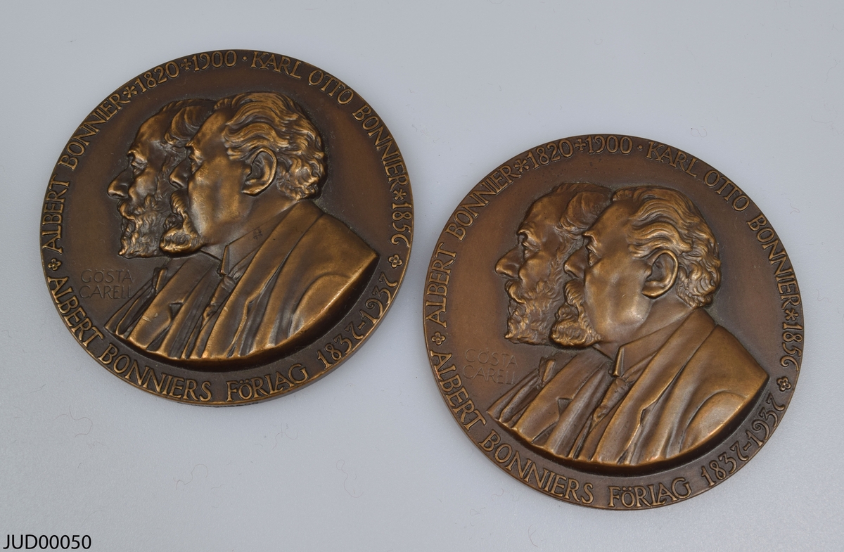 Två stycken bronsmedaljer med olika personer ur familjen Bonnier i profil på ena sidan, samt graverade ansikten på andra sidan.