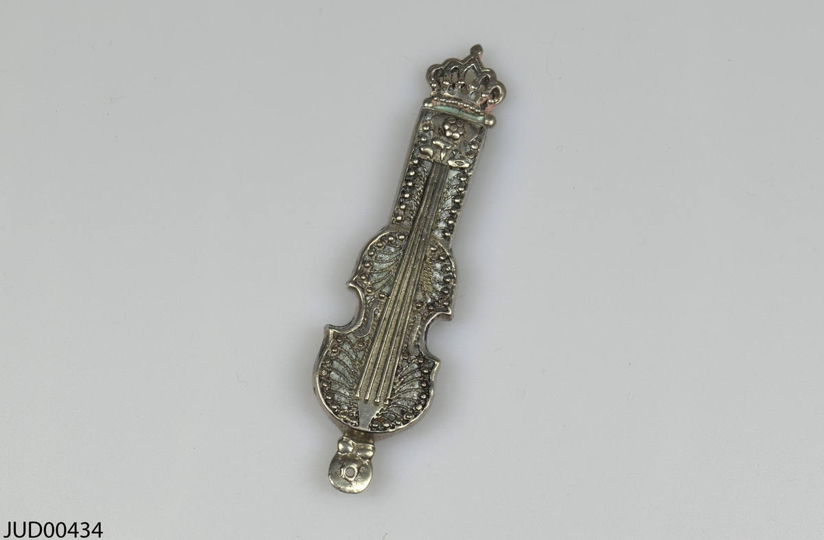 Mezuza tillverkad av silver, i form av en fiol med en krona på toppen. Fasttejpad lapp på baksidan där det står: Gåva av Elisabeth Lundmark Sthlm 1989.